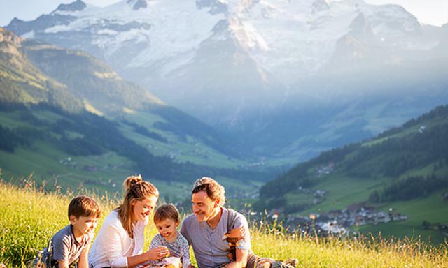 Familie auf einer grünen Schweizer Sommerwiese vor einer Bergkulisse